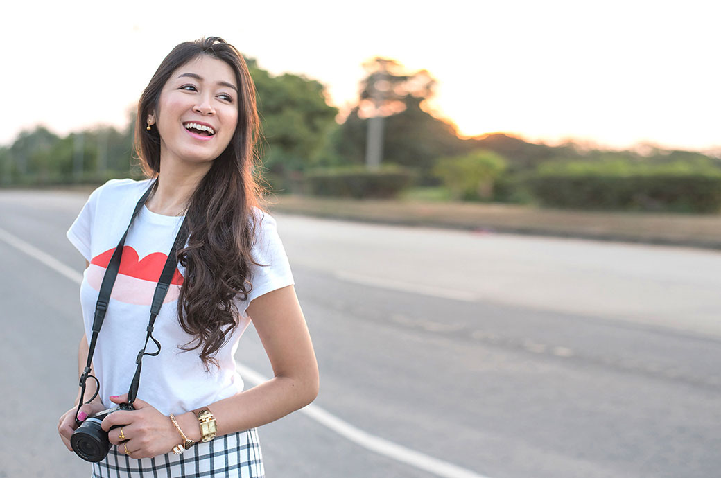 一位帶著相機的年輕女旅行者在公路上微笑